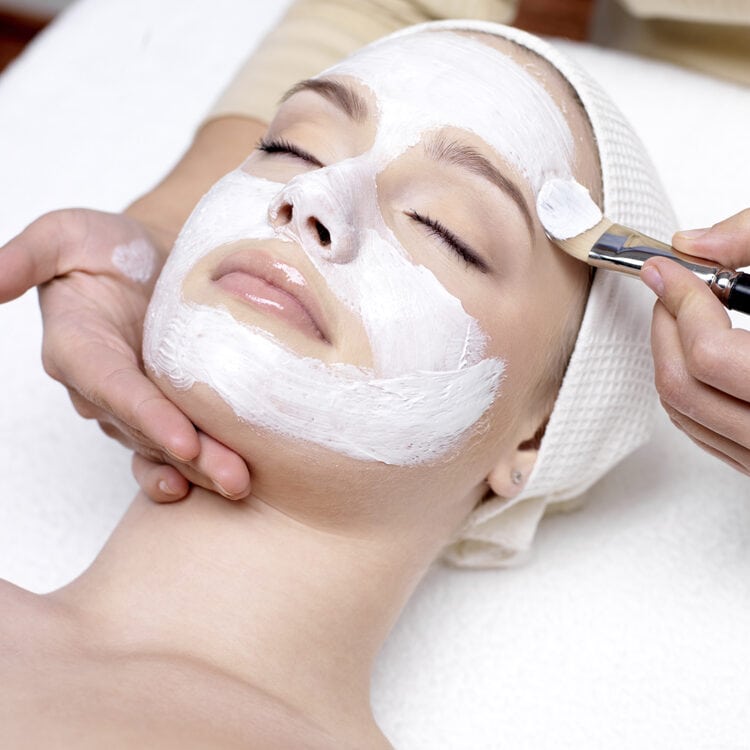 Beautiful young woman receiving facial mask at beauty salon - indoors